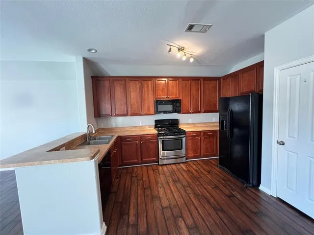 a kitchen with granite countertop wooden floors a refrigerator and wooden cabinets