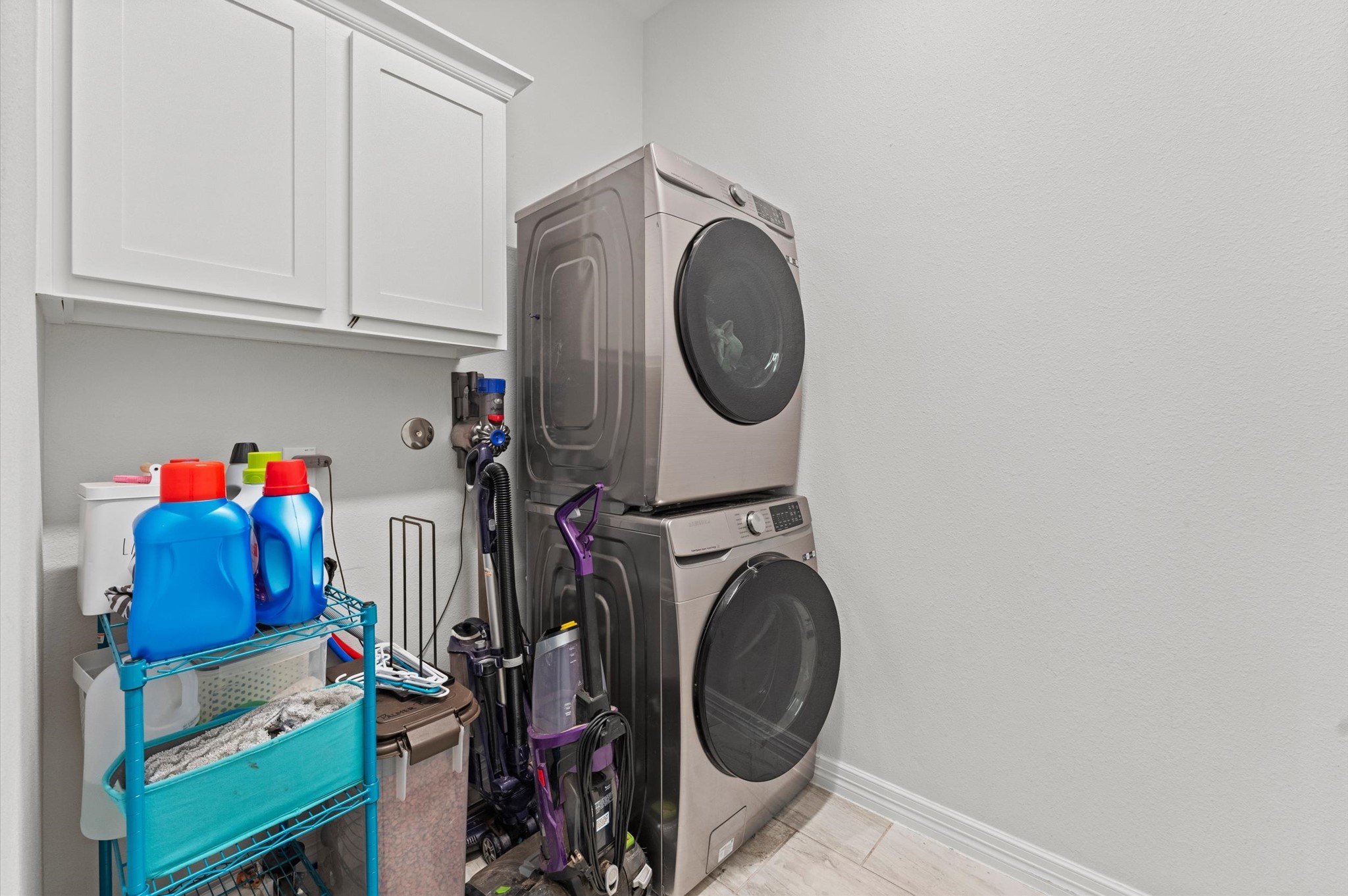 3510 Whitman Drive Rosharon, TX 77583 - Photo 16 of 25 Compact laundry room featuring a stacked washer and dryer, overhead cabinets for storage, and a small shelving unit for supplies. Perfect for efficient space utilization.