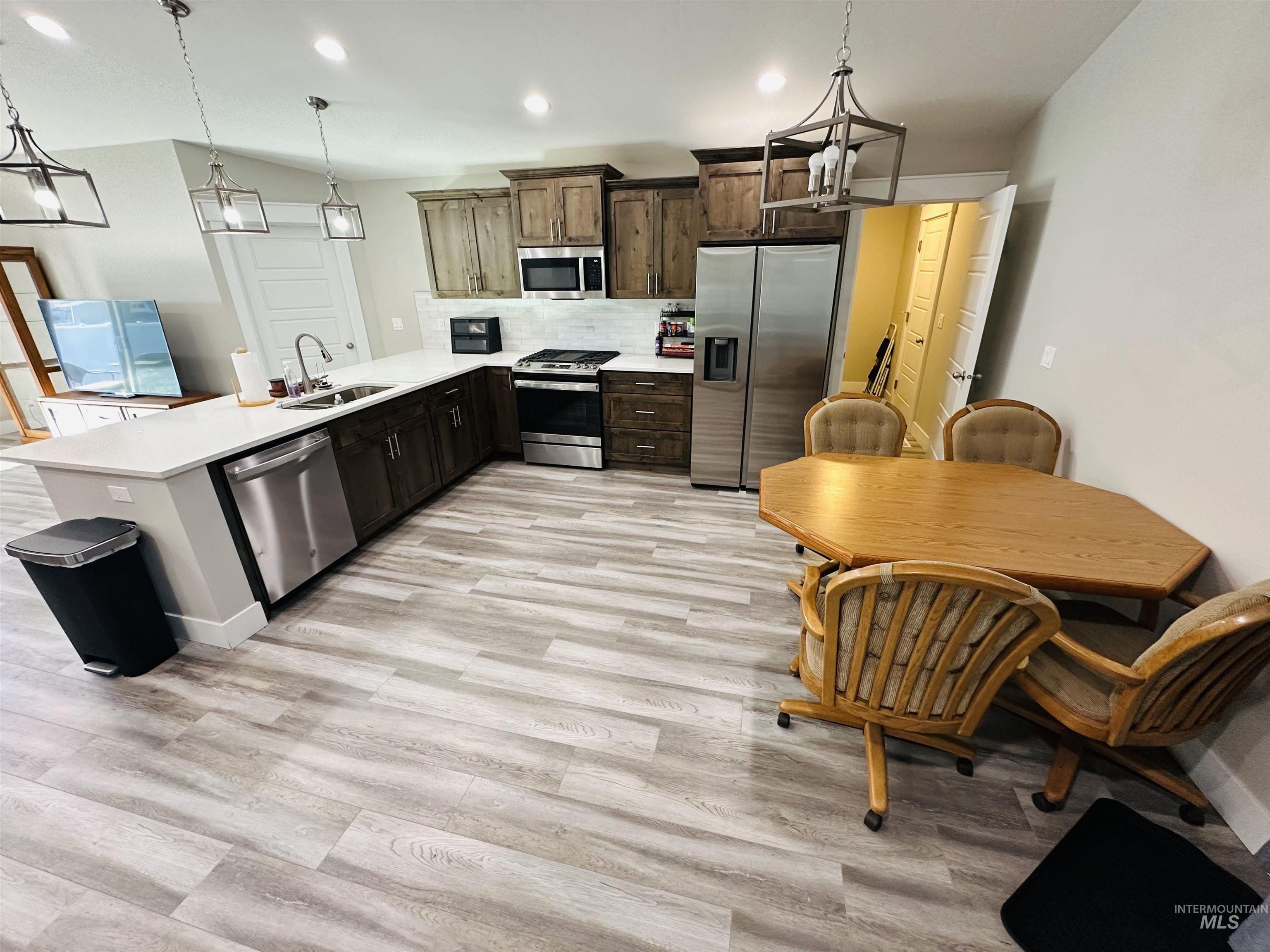 911 Campbell Street Vale, OR 97918 - Photo 4 of 37 Kitchen featuring stainless steel appliances, decorative light fixtures, backsplash, a peninsula, and light wood-type flooring