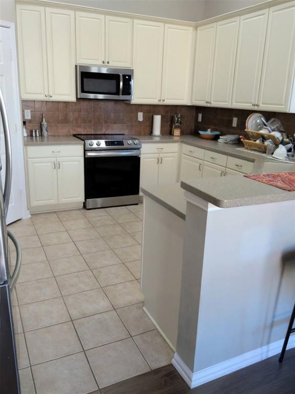 1848 Sandpiper Lane Carrollton, TX 75007 - Photo 3 of 8 Kitchen featuring appliances with stainless steel finishes, backsplash, white cabinets, and light tile patterned floors
