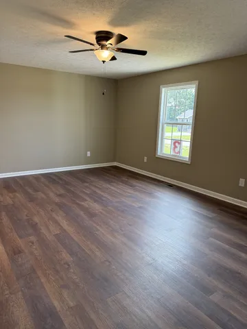 an empty room with wooden floor chandelier fan and windows