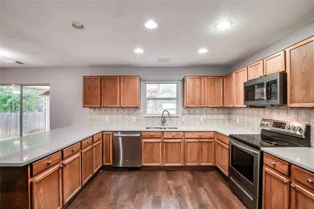 a kitchen with stainless steel appliances a sink dishwasher a stove top oven a refrigerator with wooden floors and cabinets