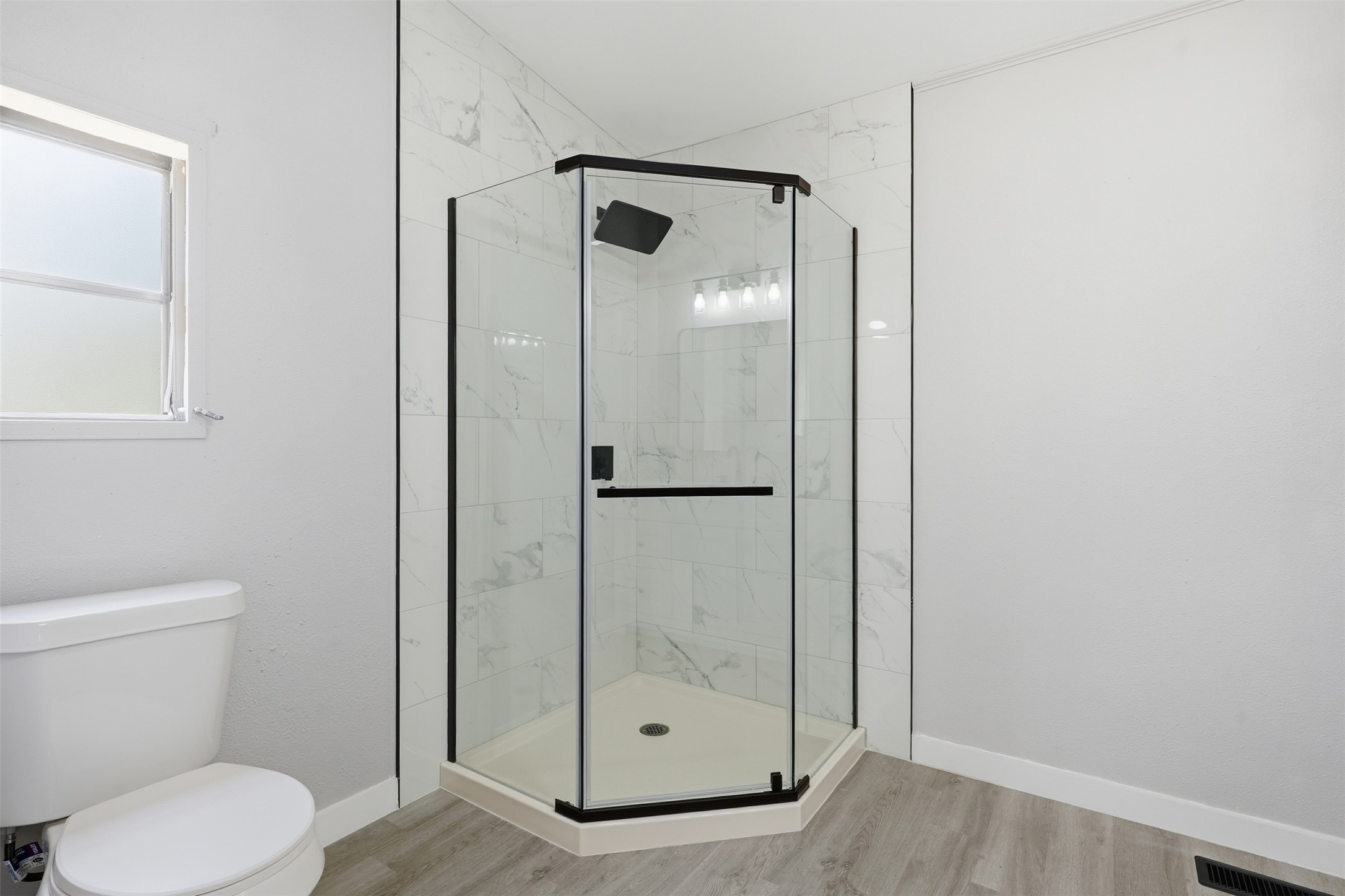 154 Antioch Road Smithville, TX 78957 - Photo 15 of 32 A well-lit primary bathroom features a corner glass-enclosed shower with tile surround and durable vinyl plank flooring.