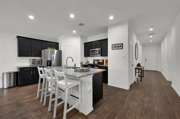 a kitchen with stainless steel appliances kitchen island granite countertop a refrigerator a stove a microwave oven a sink with island and chairs with wooden floor