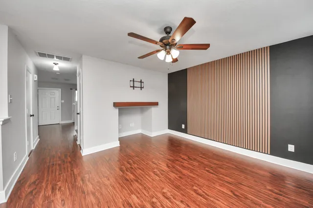 a view of an empty room and kitchen with wooden floor