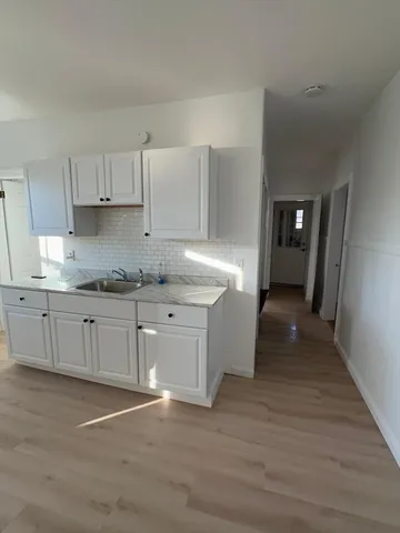 a kitchen with granite countertop a stove a sink and white cabinets with wooden floor