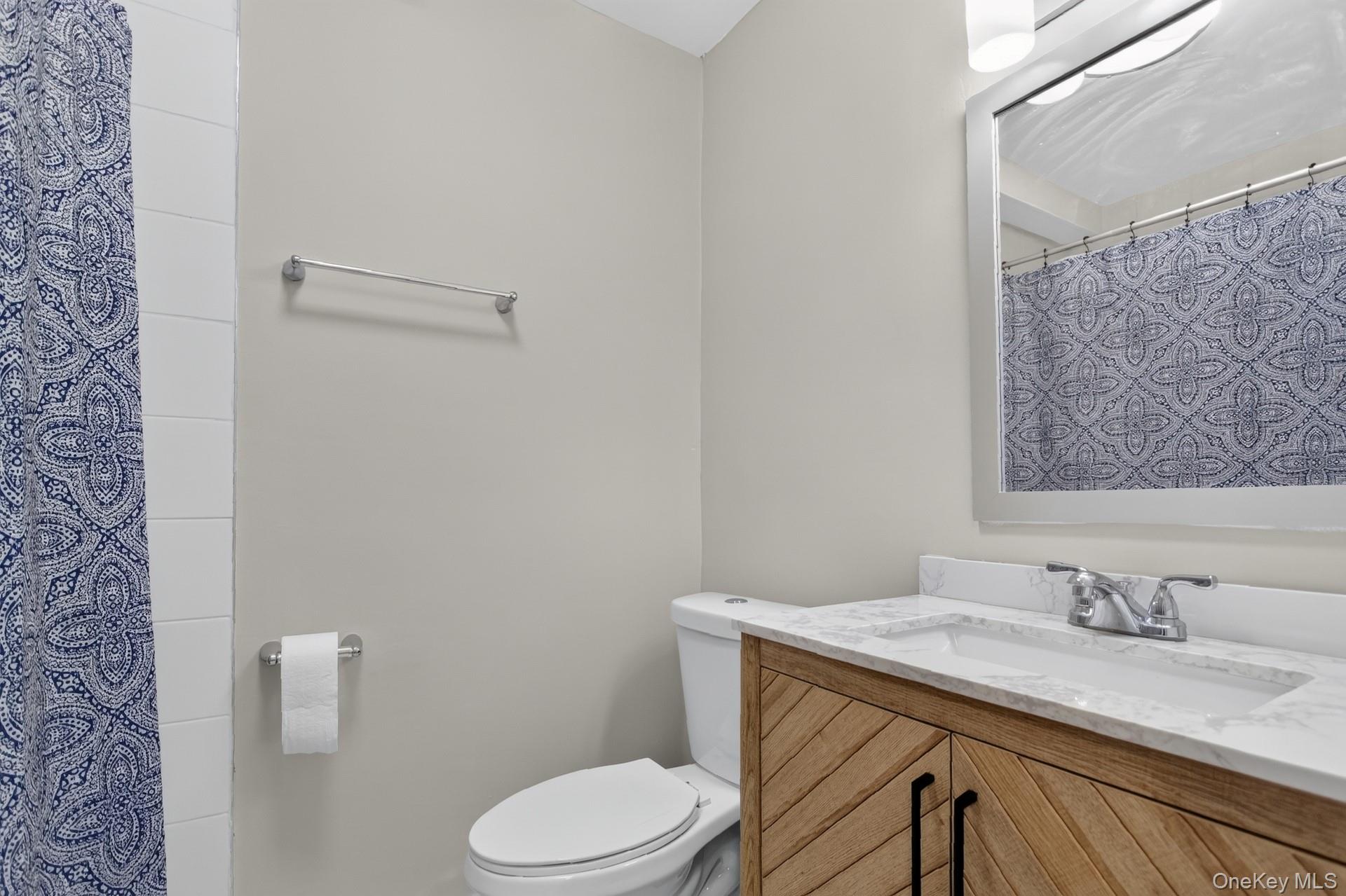 26 Cooper Road, Unit 414 Poughkeepsie, NY 12603 - Photo 21 of 24 Bathroom featuring a vanity with a white countertop and integrated sink, wood-finish cabinetry, and brushed nickel fixtures