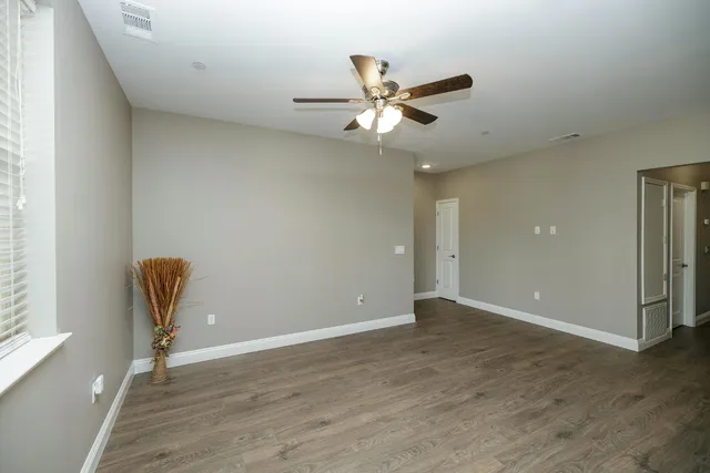 an empty room with wooden floor a ceiling fan and windows