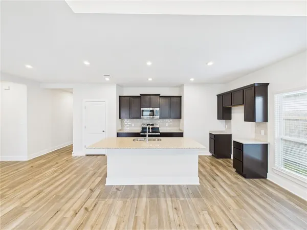 a large white kitchen with stainless steel appliances kitchen island a stove a refrigerator with cabinets and wooden floor