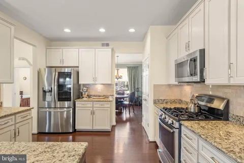 a kitchen with stainless steel appliances granite countertop a stove top oven a sink dishwasher and a refrigerator with wooden floor