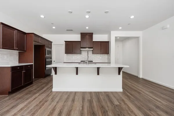 a large kitchen with stainless steel appliances a large counter top a stove and a wooden floors