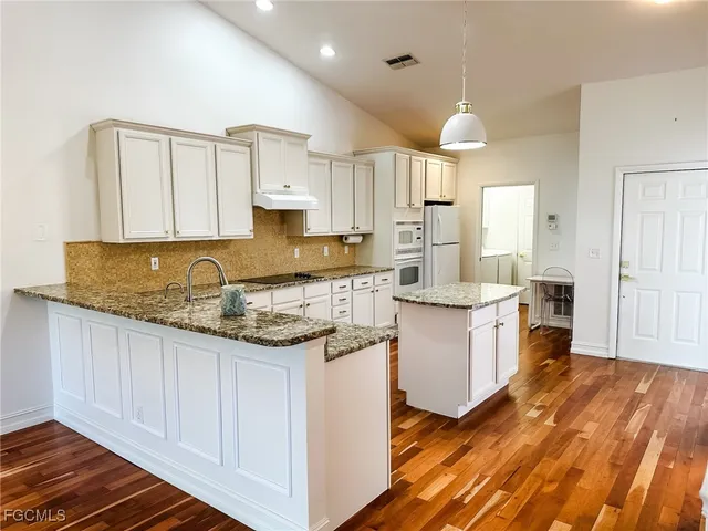 a kitchen with stainless steel appliances granite countertop a stove a sink and white cabinets with wooden floor