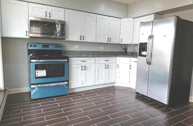 a kitchen with granite countertop a refrigerator stove and white cabinets