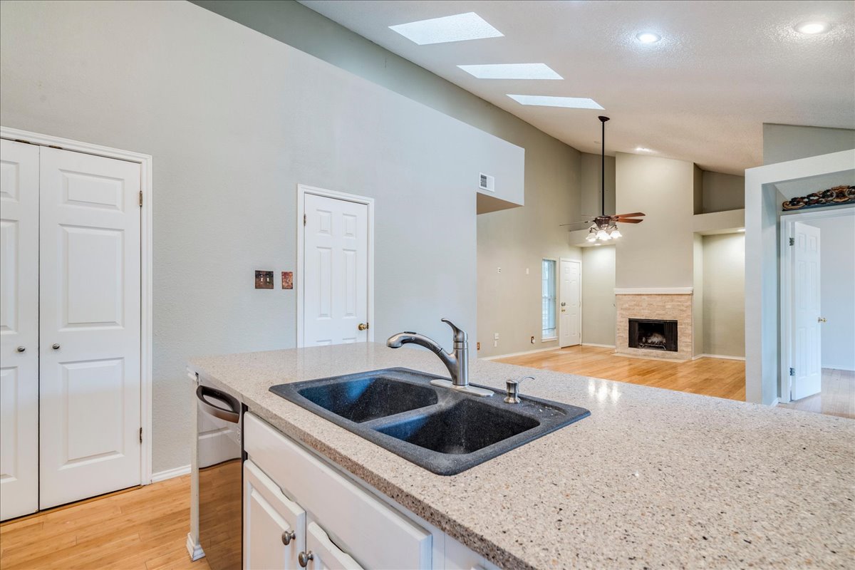 3809 Spicewood Springs Road, Unit 127 Austin, TX 78759 - Photo 11 of 29 A well-lit kitchen with stone counters overlooks a living space featuring a cozy fireplace and soaring vaulted ceilings.