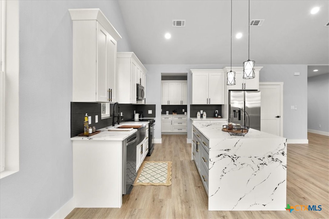 1190 Fernwood Road Fischer, TX 78623 - Photo 13 of 27 a large kitchen with kitchen island a stove a sink a refrigerator and white cabinets with wooden floor