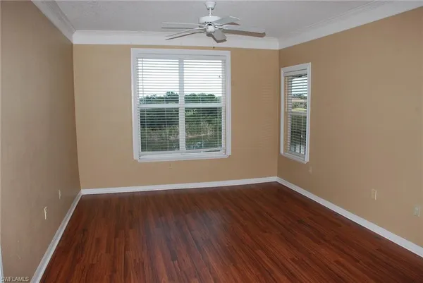 an empty room with wooden floor chandelier fan and windows
