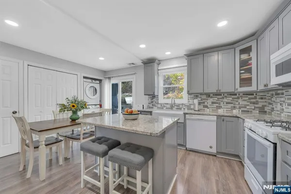 a kitchen with stainless steel appliances granite countertop a refrigerator a sink dishwasher a stove and white cabinets with wooden floor