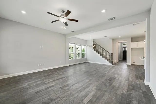 a view of an empty room with wooden floor and a ceiling fan