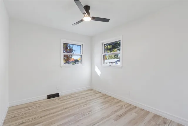 an empty room with wooden floor ceiling fan and window