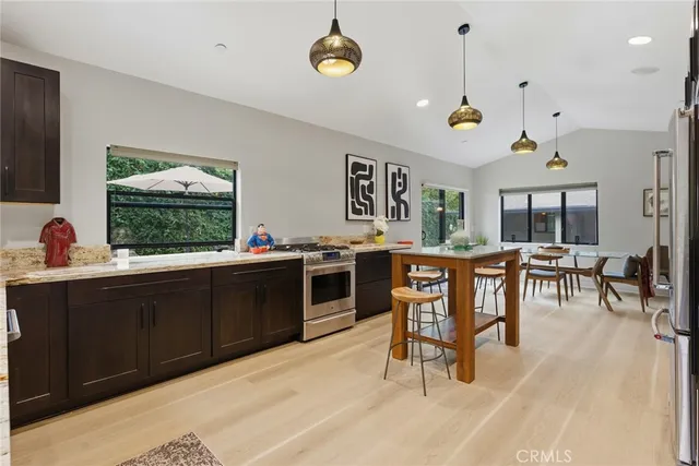 a open kitchen with stainless steel appliances granite countertop a stove top oven a sink a dining table and chairs with wooden floor