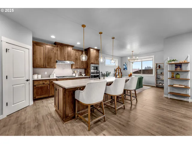 a kitchen with stainless steel appliances granite countertop a stove a refrigerator a kitchen island a dining table and chairs with wooden floor
