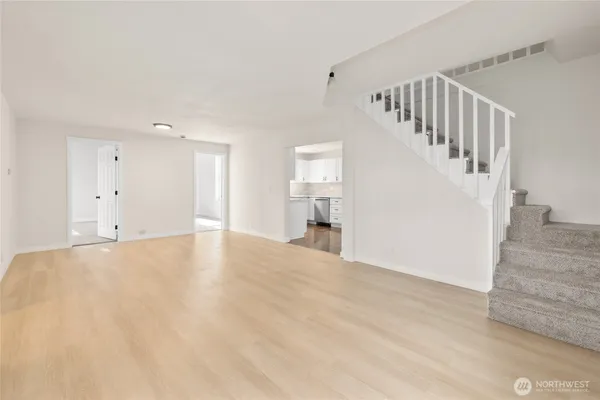 a view of an empty room with stairs and a living room