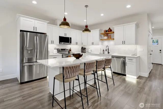 a kitchen with stainless steel appliances kitchen island granite countertop a table chairs refrigerator and microwave