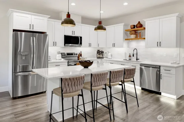 a kitchen with stainless steel appliances granite countertop a dining table chairs refrigerator and microwave