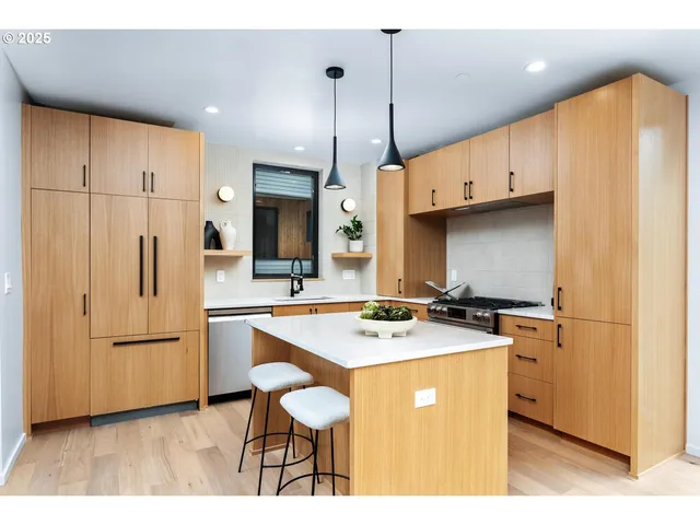 a kitchen with stainless steel appliances granite countertop a refrigerator a sink dishwasher a stove a dining table and chairs with wooden floor