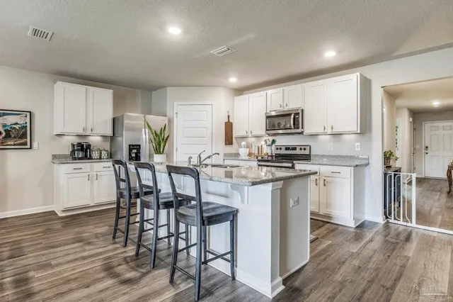 a kitchen with kitchen island granite countertop wooden floors white cabinets and stainless steel appliances