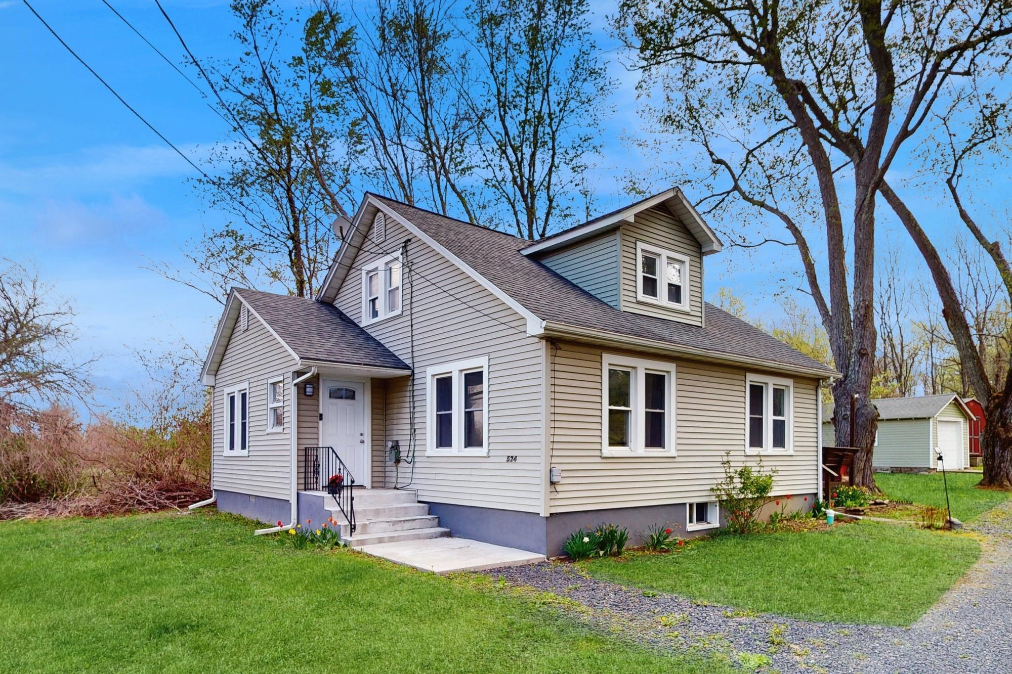 View of front facade featuring outbuildings, a shingled roof, and a front lawn.
