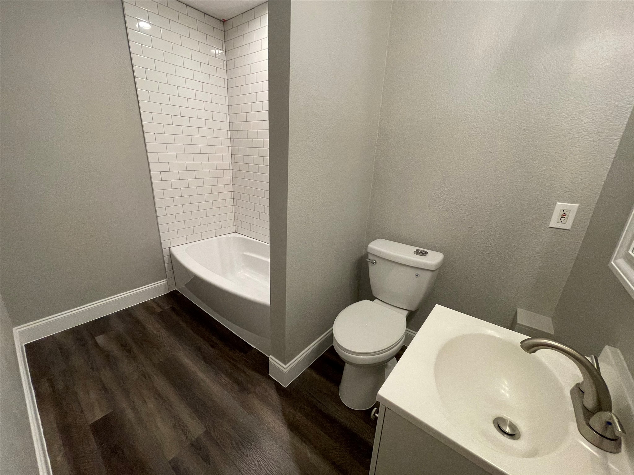 2004 Maple Street Georgetown, TX 78626 - Photo 19 of 31 Bathroom featuring a white subway tile shower surround, a white bathtub, and wood-finish flooring