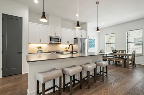 a kitchen with stainless steel appliances granite countertop a stove a refrigerator a kitchen island a dining table and chairs with wooden floor
