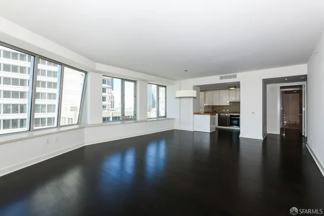 a view of empty room with wooden floor and kitchen view