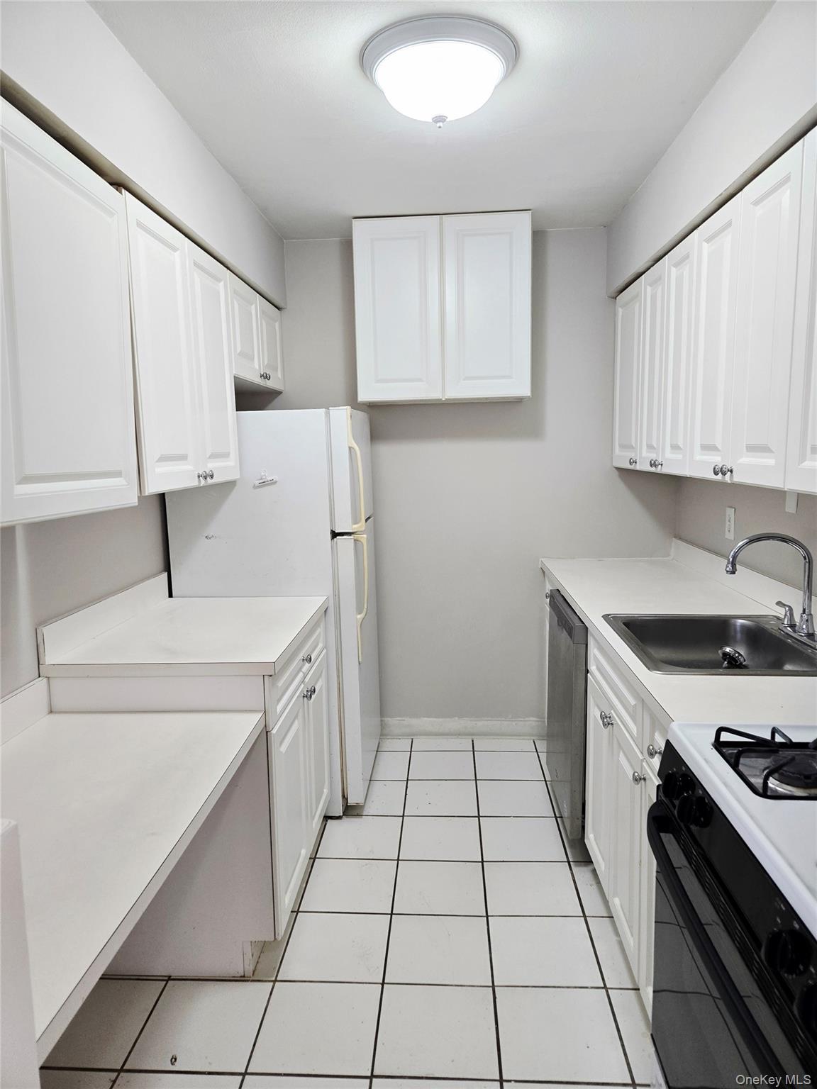 79 Pointe Circle South, Unit 79 Coram, NY 11727 - Photo 7 of 39 Kitchen with black gas range oven, light countertops, white cabinetry, freestanding refrigerator, and light tile patterned floors