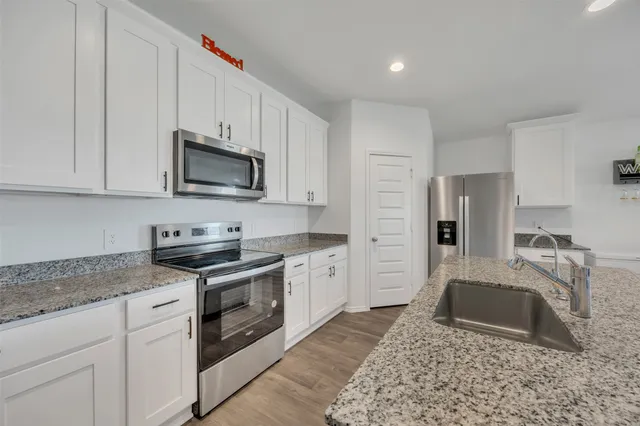 a kitchen with granite countertop a sink a stove top oven a refrigerator and cabinets