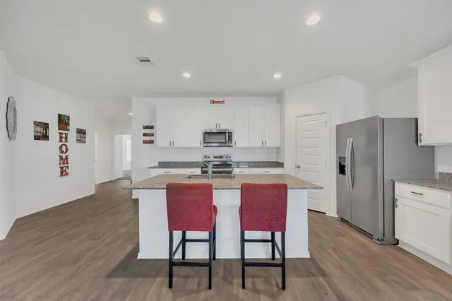 a kitchen with stainless steel appliances granite countertop a dining table chairs refrigerator and sink