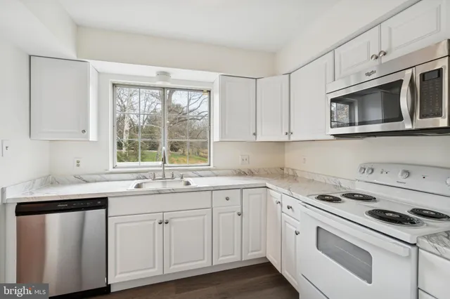 a kitchen with white cabinets appliances a sink and a window
