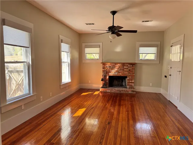 a view of an empty room with wooden floor fireplace and a window