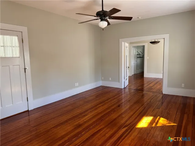 a view of empty room with wooden floor and fan