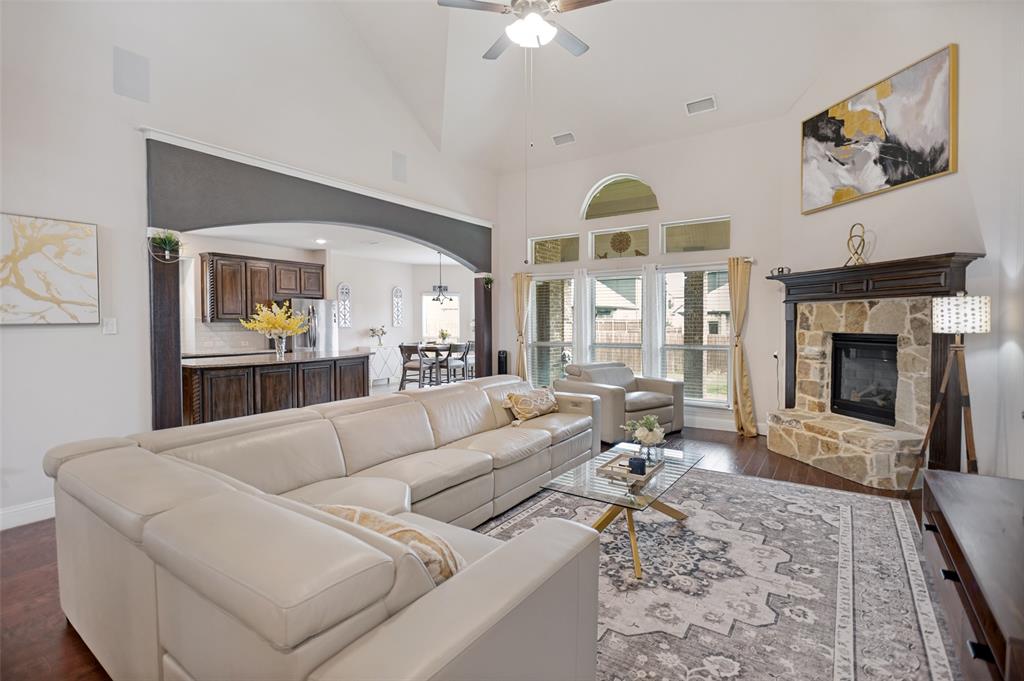 413 Frontier Court Midlothian, TX 76065 - Photo 7 of 26 Living area featuring vaulted ceilings, an arched entryway to the kitchen, wood-finish flooring, a stone fireplace with a dark wood mantel, and large windows with an arched transom