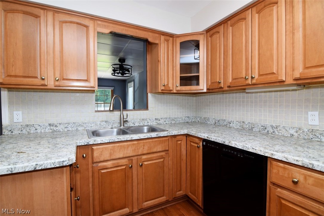 5284 Edenhurst Road Lyndhurst, OH 44124 - Photo 15 of 50 Wood-finish cabinetry with brass hardware, light-toned solid surface countertops, square tile backsplash, and a stainless steel double basin sink with a gooseneck faucet