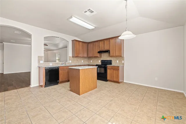 a kitchen with a stove a sink a center island a counter top space and cabinets