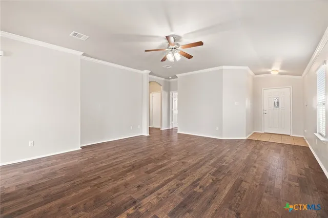 a view of an empty room with wooden floor and a ceiling fan
