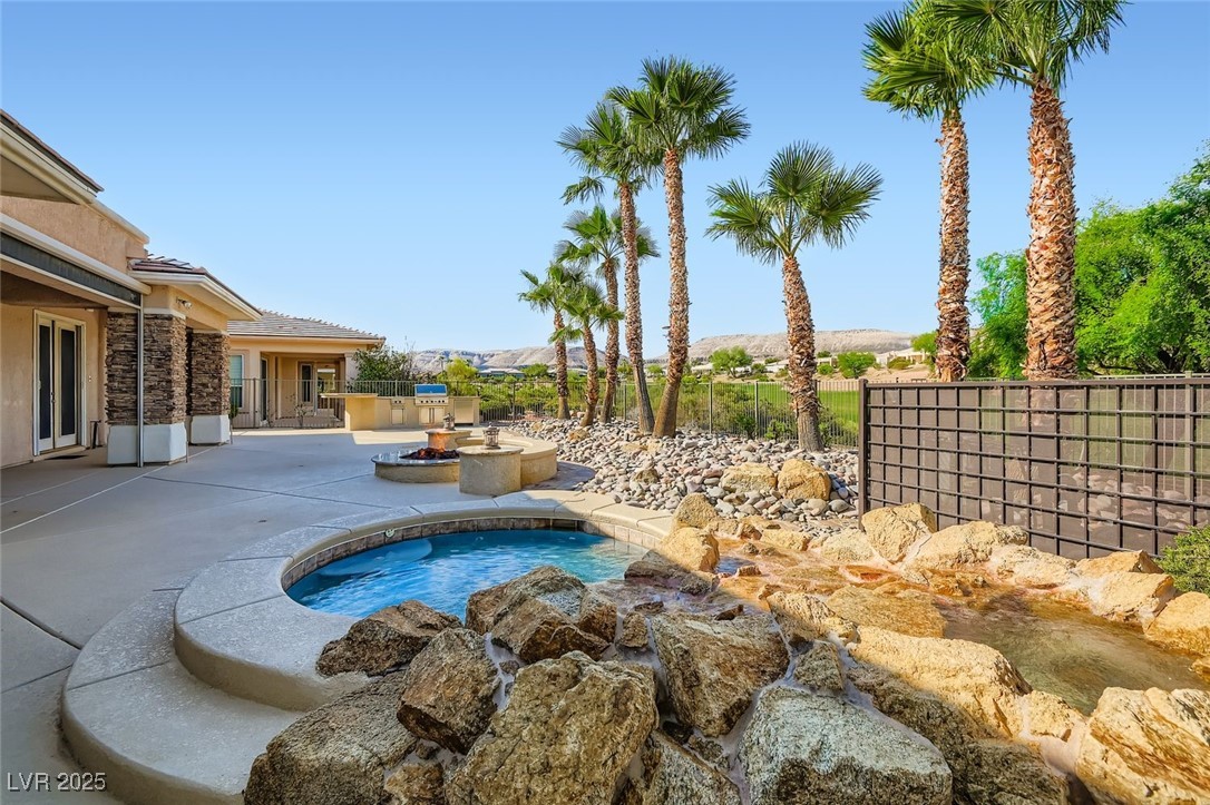 5015 Rivedro Street Las Vegas, NV 89135 - Photo 1 of 63 This back patio view highlights the inviting spool, cozy gas firepit, and a full outdoor kitchen at the far end—ideal for entertaining or unwinding. The meticulously maintained landscaping is among the finest in the community, framing breathtaking views of the 15th fairway at Siena Golf Course and the majestic Sierra Nevada Mountains beyond.