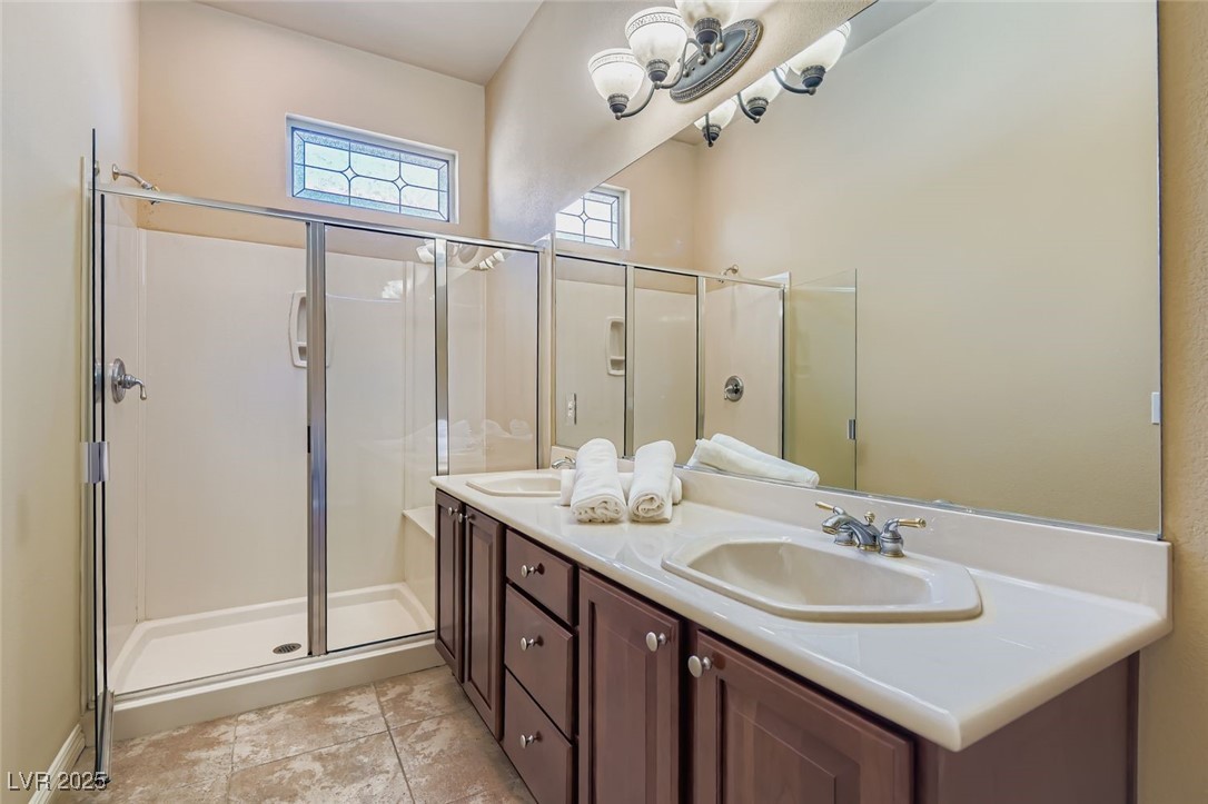 5015 Rivedro Street Las Vegas, NV 89135 - Photo 11 of 63 This spacious bath features a double vanity, a sleek shower stall, and light tile-patterned flooring that adds a clean, modern touch. Above the shower, custom stained glass brings in soft natural light while adding a distinctive artistic accent to the space.