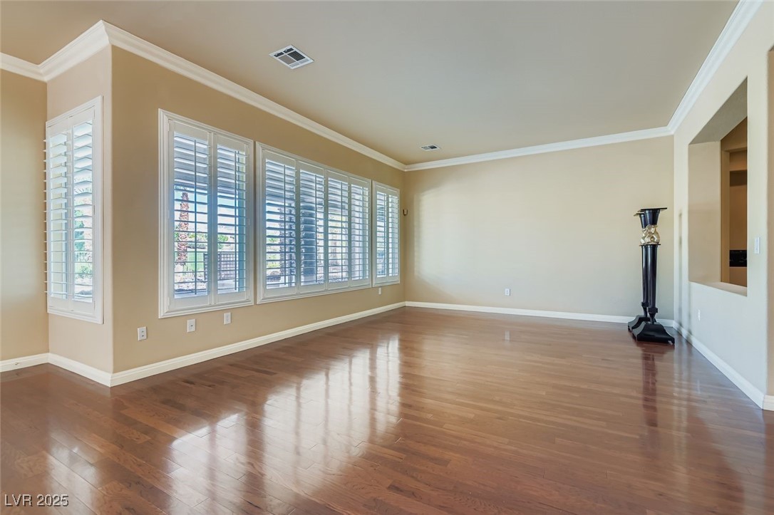 5015 Rivedro Street Las Vegas, NV 89135 - Photo 17 of 63 This inviting living room showcases timeless plantation shutters, rich crown molding, and warm hardwood-style flooring—creating a perfect blend of comfort and sophistication.