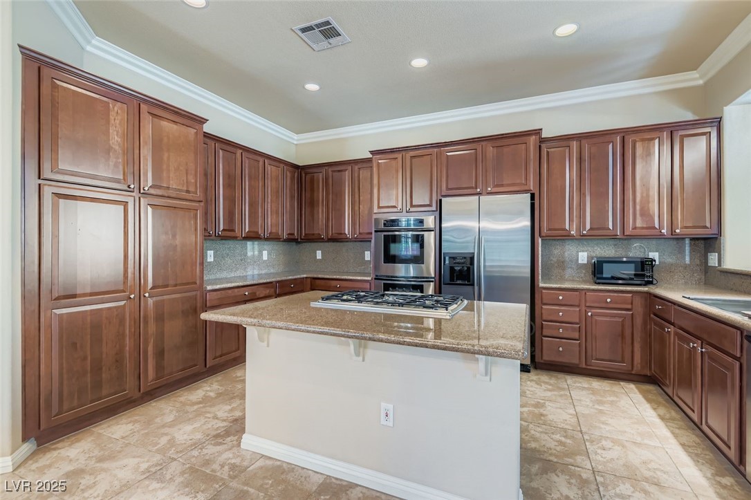 5015 Rivedro Street Las Vegas, NV 89135 - Photo 20 of 63 This beautifully appointed kitchen features a central island for gathering and prep, crown molding for architectural charm, and a decorative backsplash that adds texture and style. Stainless steel appliances complement the light tile-patterned floors, while upgraded cabinetry offers abundant storage with a polished finish.