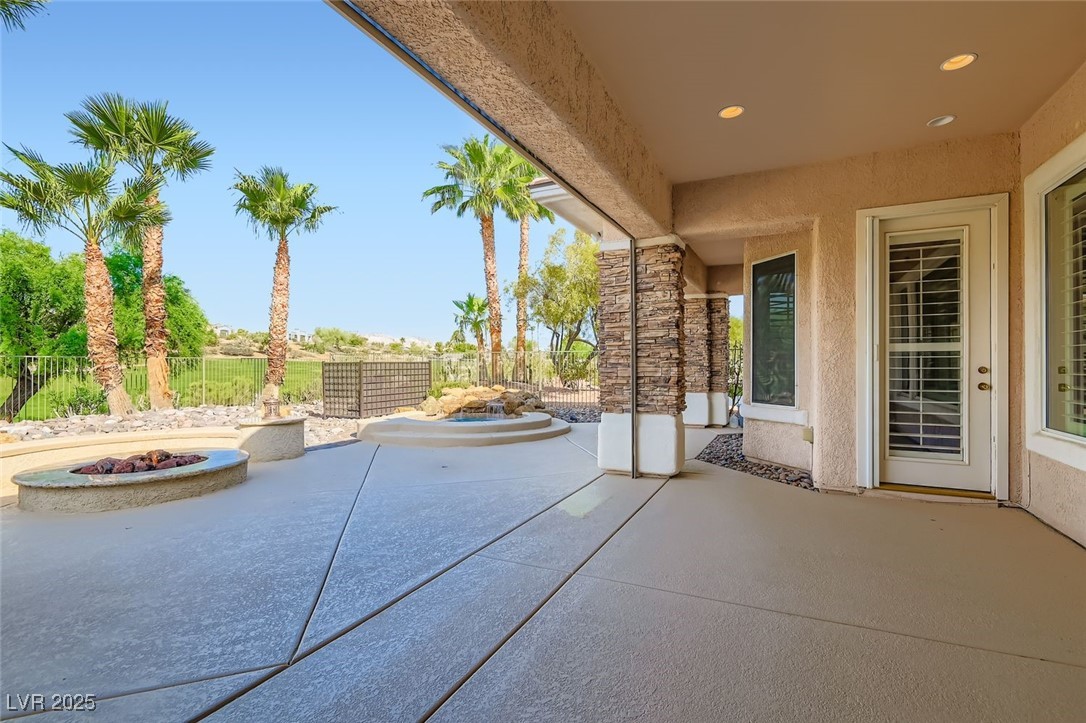5015 Rivedro Street Las Vegas, NV 89135 - Photo 25 of 63 This expansive patio and terrace area features a relaxing spool, a cozy fire pit, and a fully equipped outdoor kitchen at the far end—perfect for entertaining or unwinding. Elegant stone-sided pillars frame the space with timeless charm, while the entry door to the primary bedroom offers seamless indoor-outdoor flow.