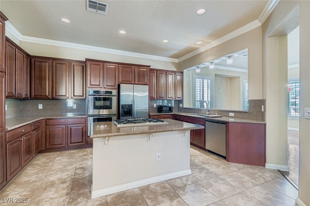 5015 Rivedro Street Las Vegas, NV 89135 - Photo 6 of 63 This beautifully appointed kitchen features a central island for gathering and prep, crown molding for architectural charm, and a decorative backsplash that adds texture and style. Stainless steel appliances complement the light tile-patterned floors, while upgraded cabinetry offers abundant storage with a polished finish.